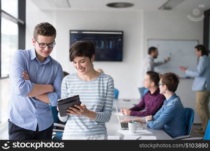 two business people using tablet preparing for next meeting and discussing ideas with colleagues in the background