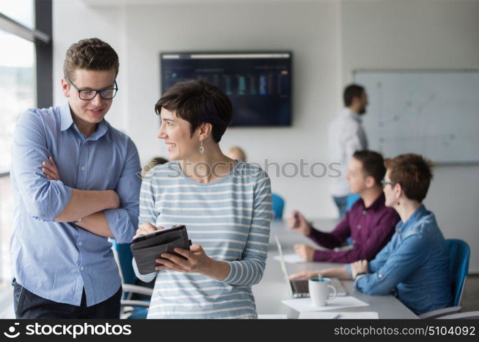 two business people using tablet preparing for next meeting and discussing ideas with colleagues in the background