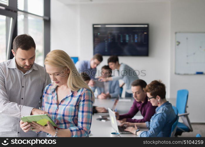 two business people using tablet preparing for next meeting and discussing ideas with colleagues in the background