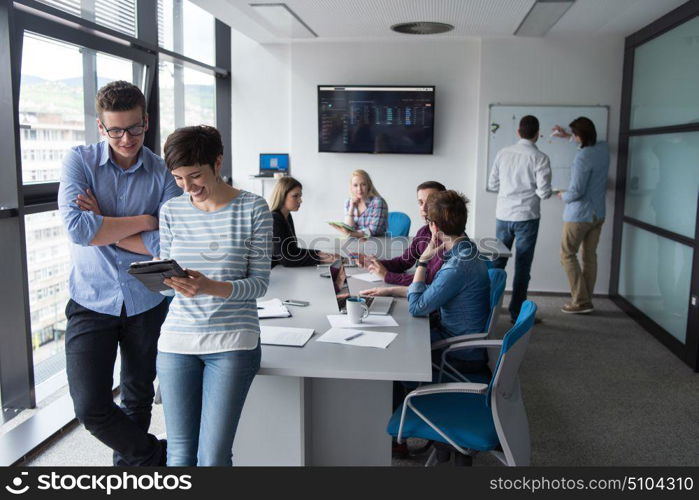 two business people using tablet preparing for next meeting and discussing ideas with colleagues in the background