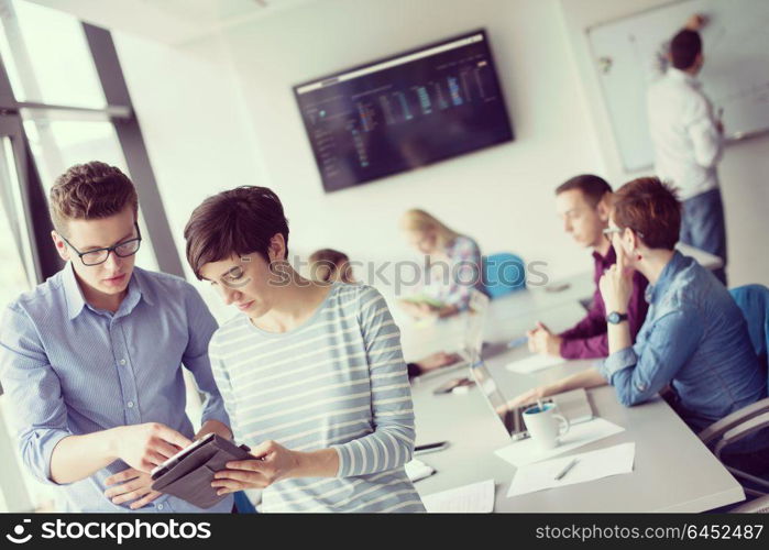 two business people using tablet preparing for next meeting and discussing ideas with colleagues in the background