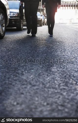 Two business people walking down a city street, legs only