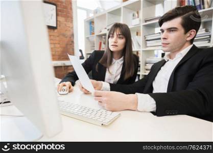 Two business people working together with documents sitting in front of computer monitor in office. Business people working together