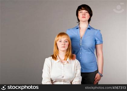 two business women, one is sitting on chair, another is standing nearby
