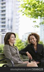 Two business women sitting on park bench, smiling