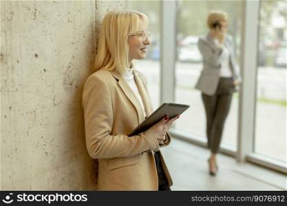 Two business women standing with laptop and mobile phone in the office corridor