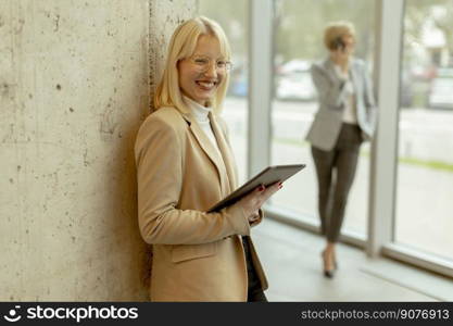 Two business women standing with laptop and mobile phone in the office corridor