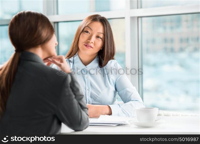 Two business women talking and signing contract at office