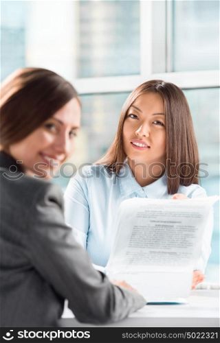 Two business women talking and signing contract at office