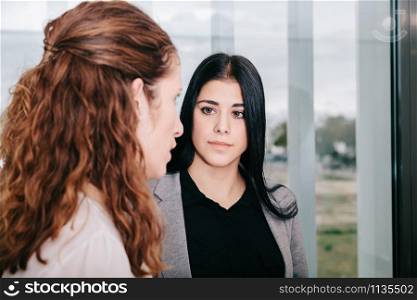 Two business women talking near a window in the office