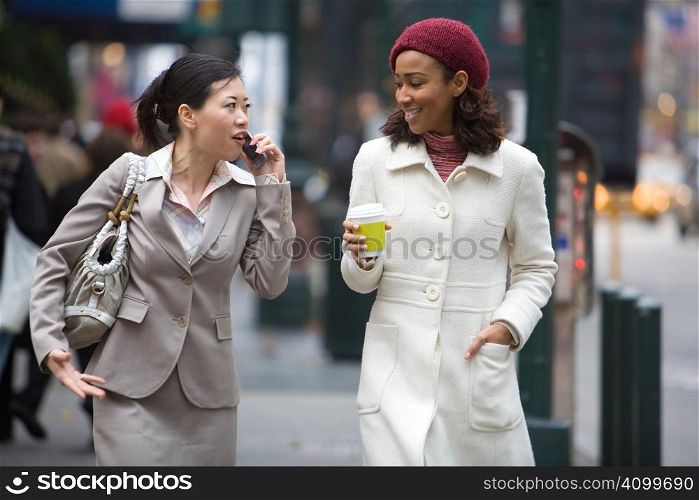 Two business women walking in the big city. One is on her cell phone.