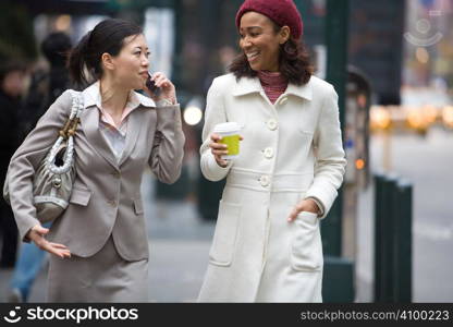 Two business women walking in the big city. One is on her cell phone.