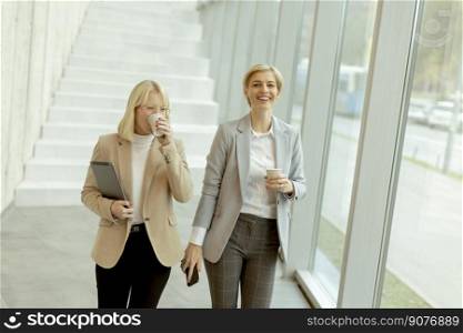Two business women walking with digital tablet and mobile phone in the office corridor