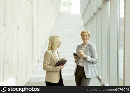 Two business women walking with digital tablet and mobile phone in the office corridor