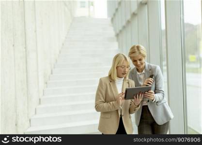 Two business women walking with laptop and mobile phone in the office corridor