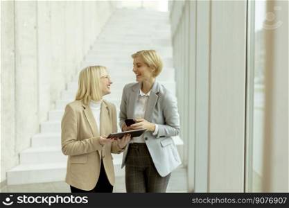 Two business women walking with laptop and mobile phone in the office corridor