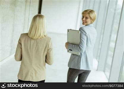 Two business women walking with laptop in the office corridor