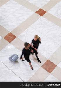 Two business women walking with suitcase elevated view long exposure