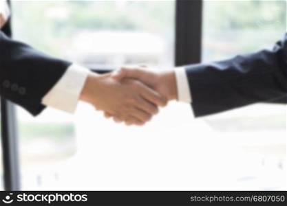 two businessman shaking hands beside window - business teamwork, cooperation concept - blur for use as background