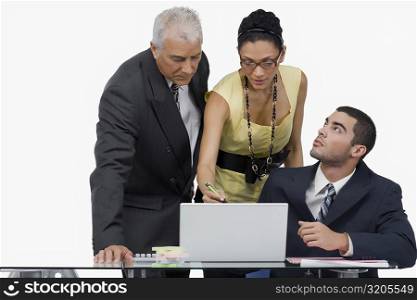 Two businessmen and a businesswoman discussing on a laptop in an office