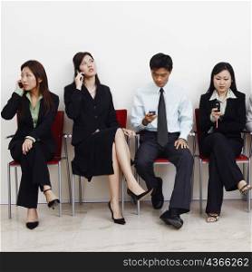 Two businessmen and three businesswomen sitting with mobile phones