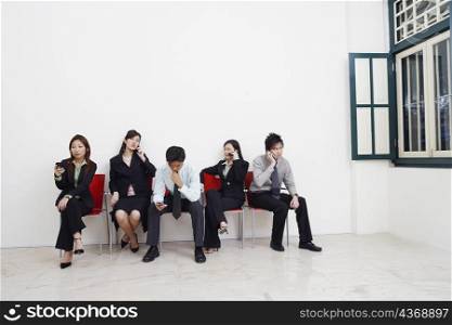 Two businessmen and three businesswomen sitting with mobile phones