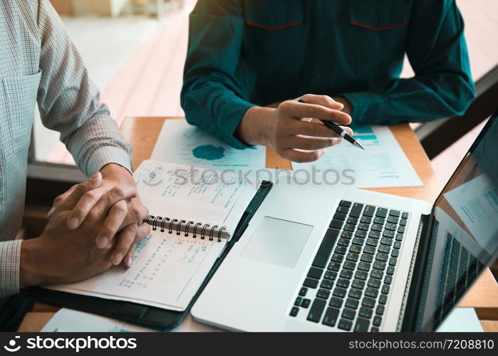 Two businessmen are together analyzing the financial data graph and pointing to the laptop computer screen.