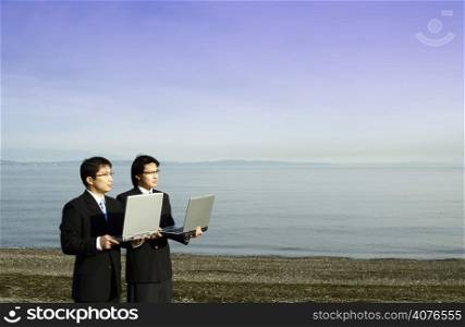 Two businessmen carrying their laptops at the beach
