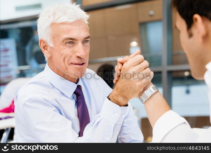 Two businessmen competeting arm wrestling in office. Who is the leader