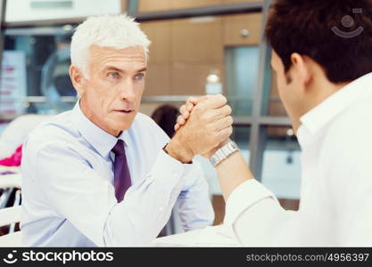 Two businessmen competeting arm wrestling in office. Who is the leader