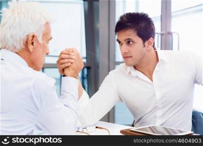 Two businessmen competing arm wrestling in office. Who is the leader