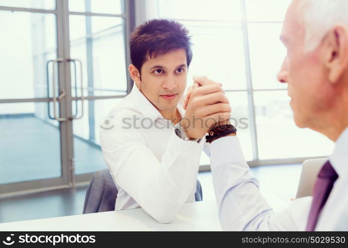 Two businessmen competing arm wrestling in office. Who is the leader