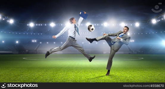 Two businessmen fight for ball. Young businessman in suit playing football at stadium