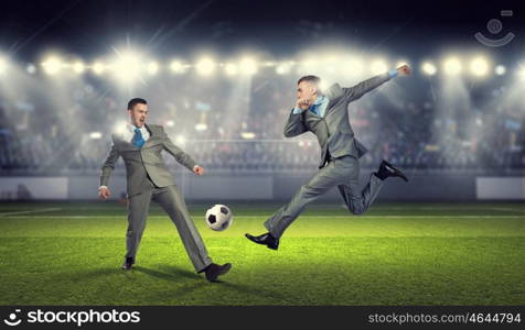 Two businessmen fight for ball. Young businessman in suit playing football at stadium