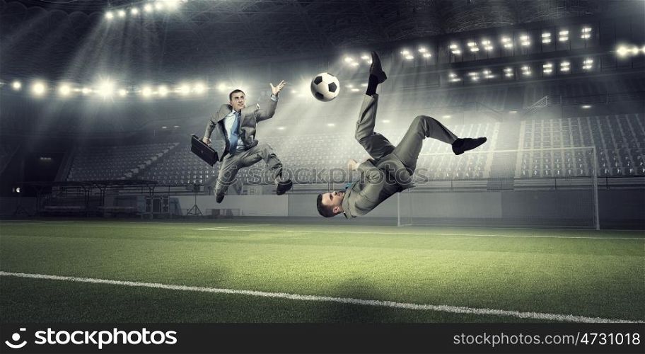 Two businessmen fight for ball. Young businessman in suit playing football at stadium