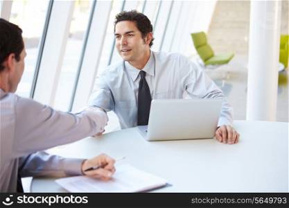 Two Businessmen Having Meeting Around Table In Modern Office