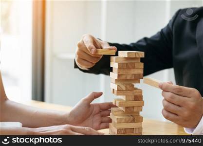 Two businessmen help to hold the wood block to fall down.