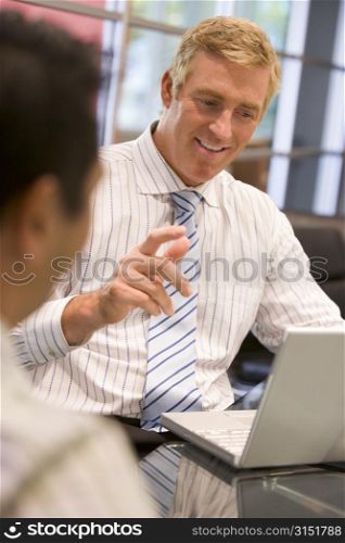 Two businessmen in boardroom with laptop talking
