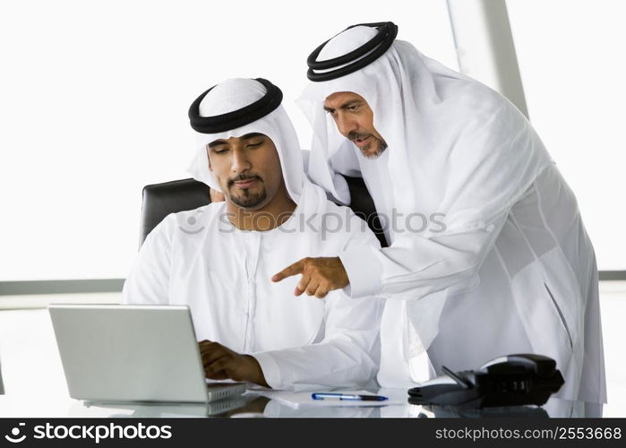 Two businessmen in office pointing at laptop (high key/selective focus)