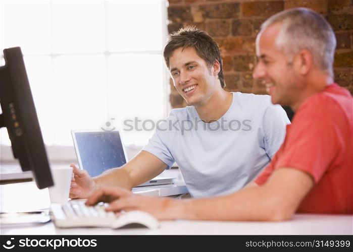 Two businessmen in office typing on computer and smiling