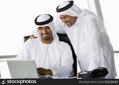 Two businessmen in office with laptop smiling (high key/selective focus)