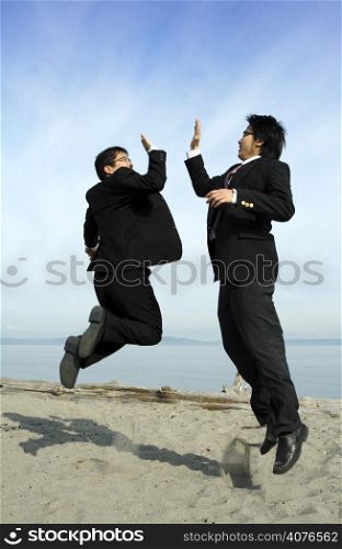 Two businessmen jumping happily on the beach