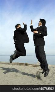 Two businessmen jumping happily on the beach