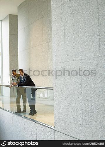 Two businessmen leaning on railing in office building