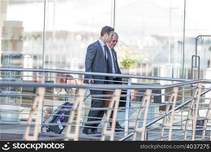 Two businessmen leaving hotel with wheeled suitcases