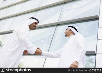 Two businessmen outdoors by building shaking hands and smiling