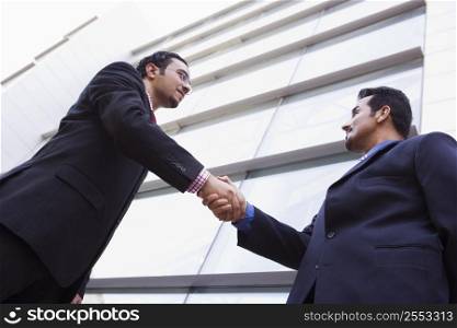 Two businessmen outdoors by building shaking hands (high key/selective focus)