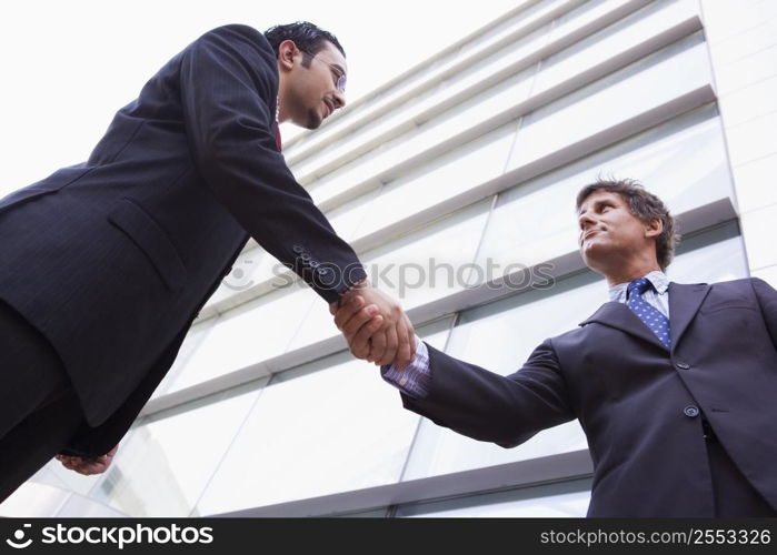 Two businessmen outdoors by building shaking hands (high key/selective focus)