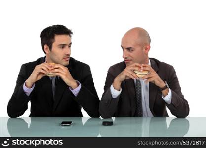Two businessmen sat eating hanburgers