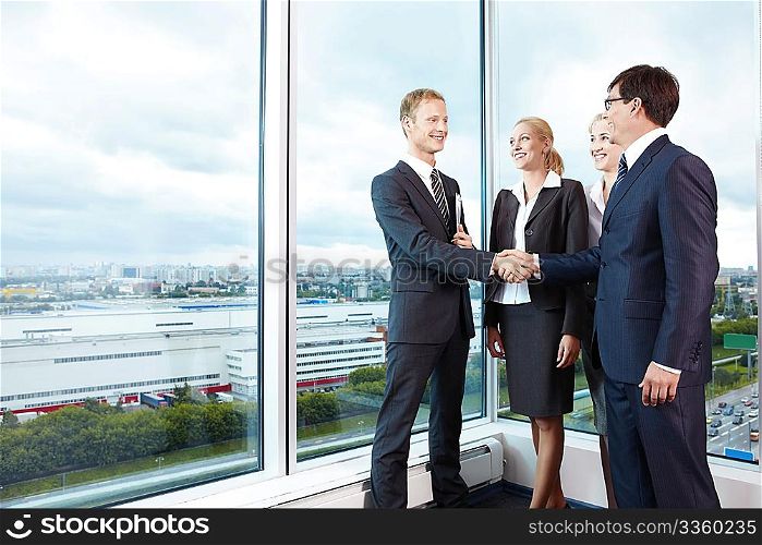 Two businessmen shake hands next to business women